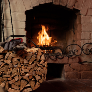 a wood fireplace burning with a big piles of logs next to it