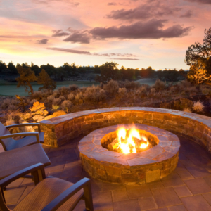 a fire pit surrounded by a low brick wall and chairs with a view of a forest in the background