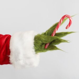 a green fuzzy Grinch hand with a Santa sleeve holding a candy cane