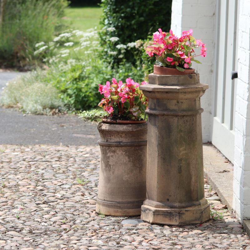 two chimney pots being used as flower pots outside a home