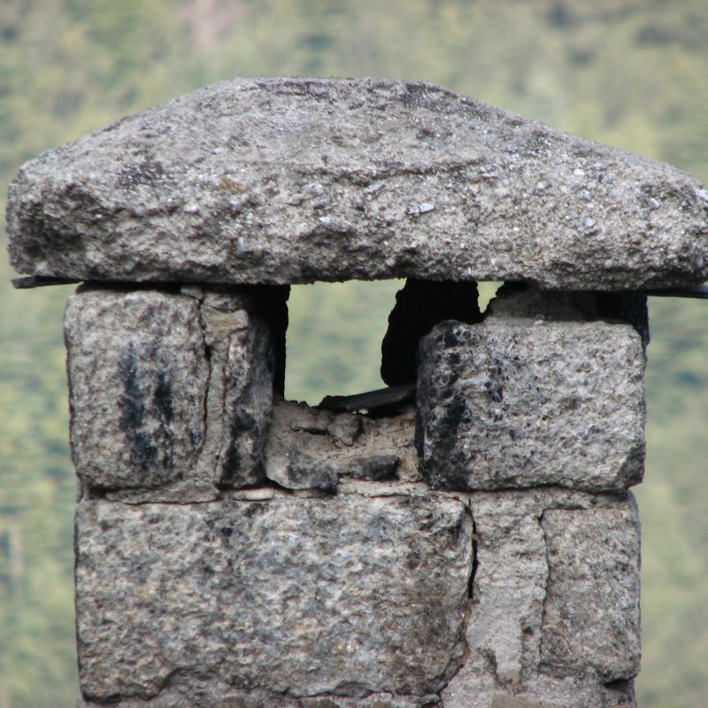 old gray stone chimney that has damage